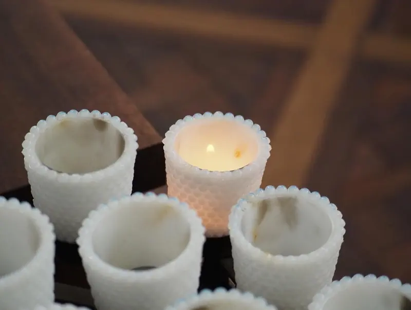 Rows of white glass votive holders, one lit