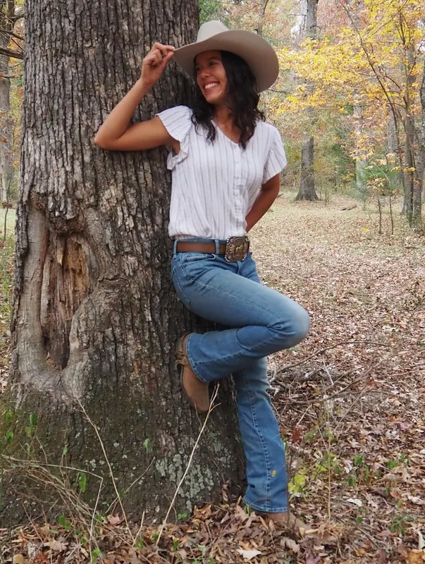 Woman in a cowboy hat leaning against a big tree in autumn woods
