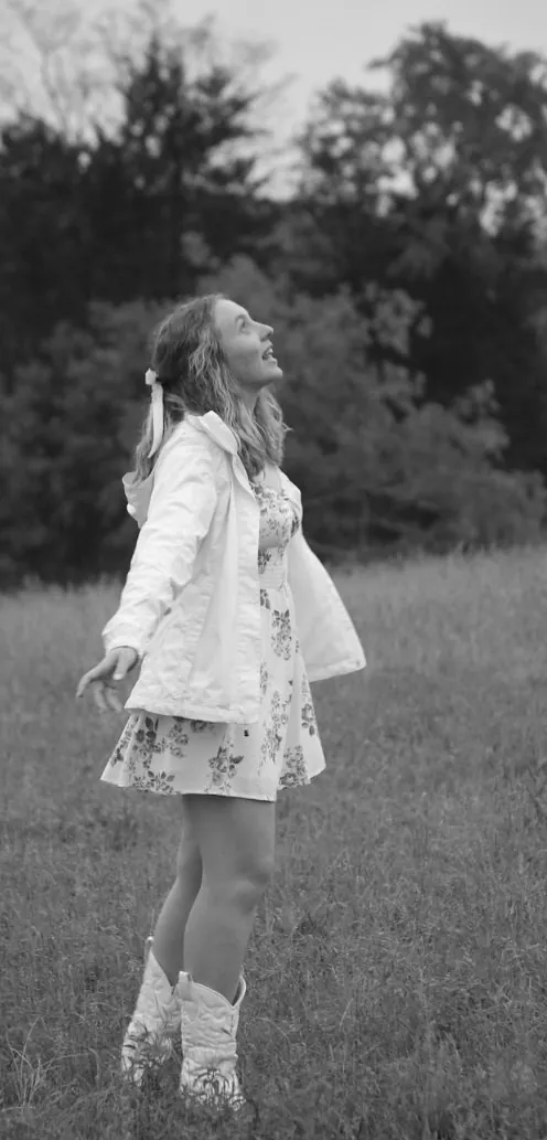 Black and white photo of Maria in a field, arms out, looking up at the sky