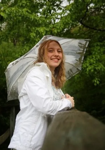 Maria smiling under a clear umbrella in the rain