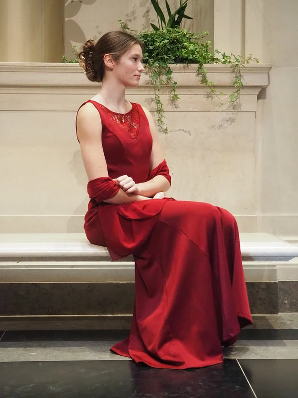 Young woman in a long red dress seated on a stone bench