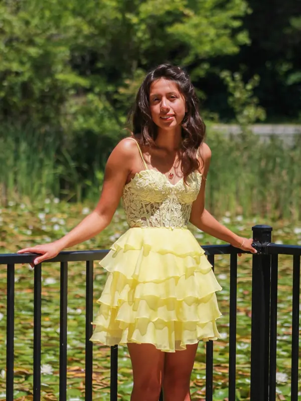Quinceañera in a short tiered yellow dress leaning on a railing by a lily pond
