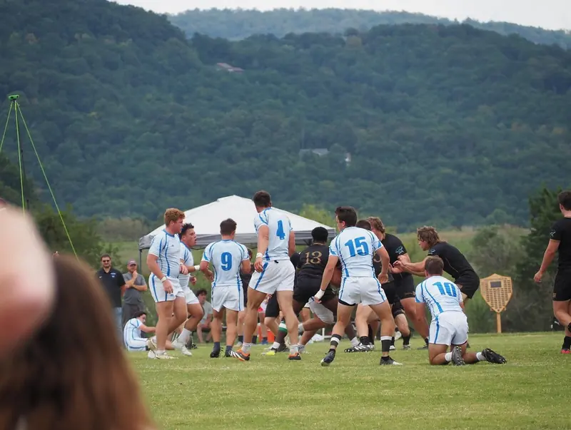 Rugby players in a ruck on a field in front of green hills