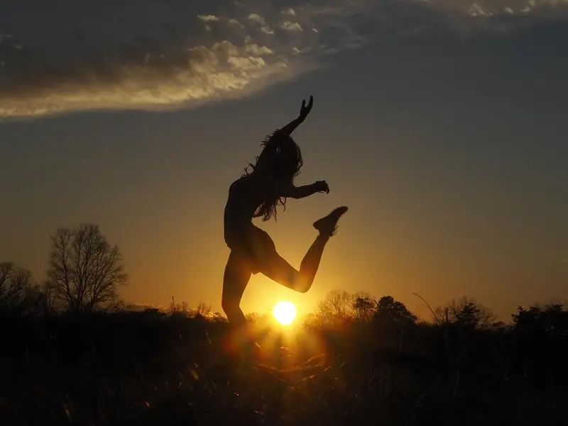 Silhouette of a dancer leaping against a golden sunset over a field
