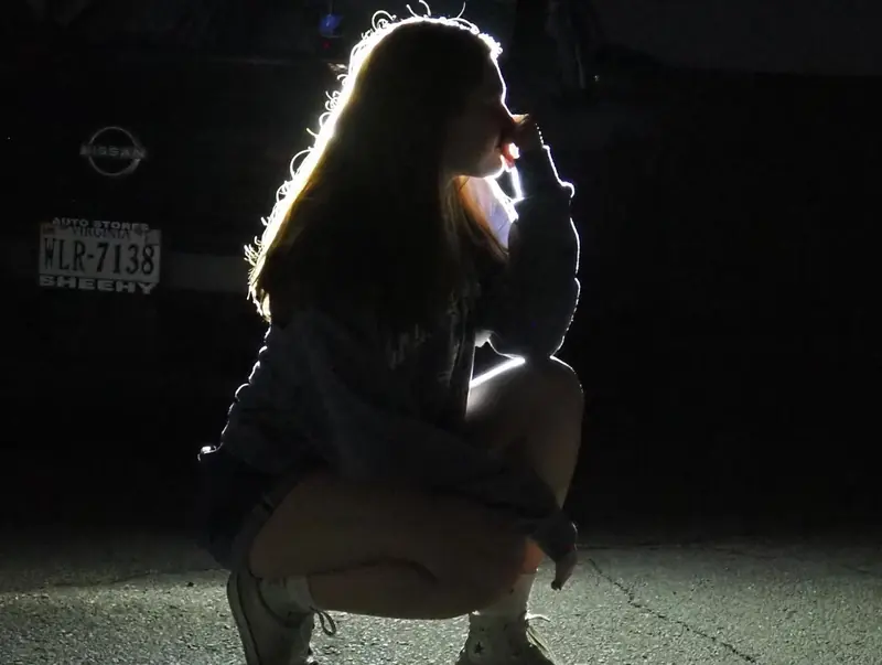Girl crouching at night, her hair rim-lit by car headlights