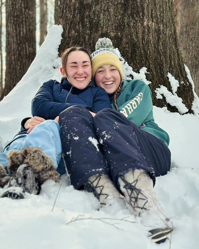 Two friends laughing together sitting in the snow