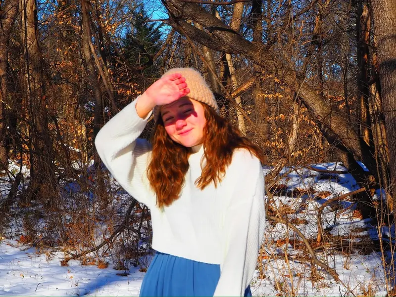 Girl in a beanie shading her eyes from the winter sun in snowy woods