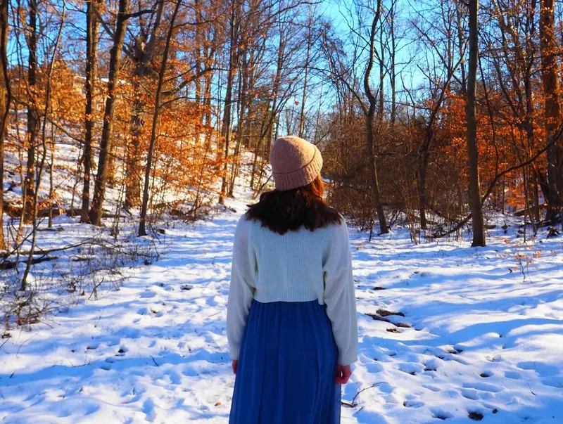 Girl in a long blue skirt walking away down a snowy forest path