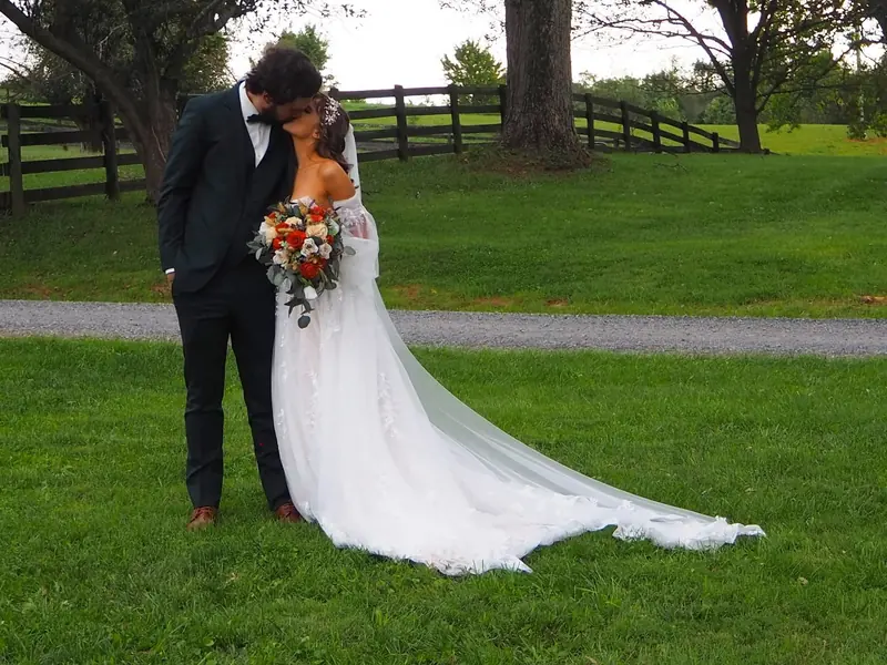 Bride and groom kissing on a green lawn, her long train spread across the grass