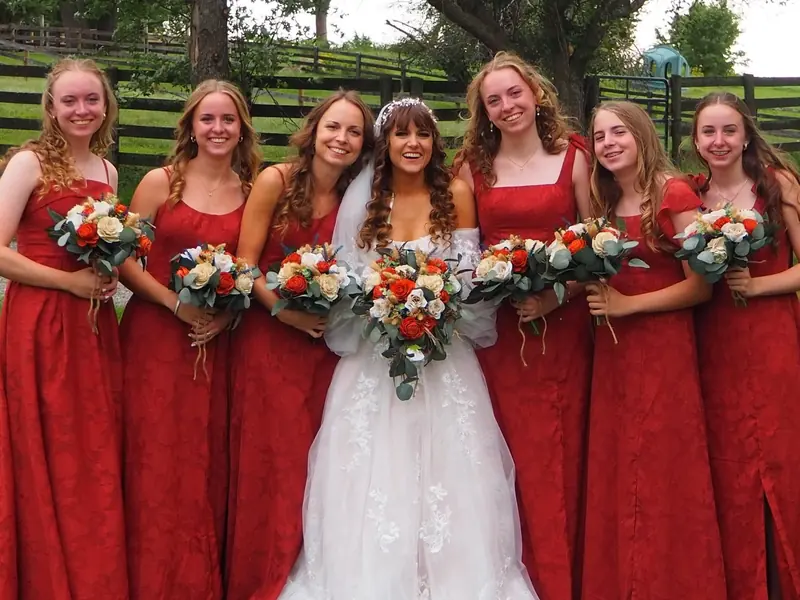 Bride with her bridesmaids in red dresses holding orange and white bouquets