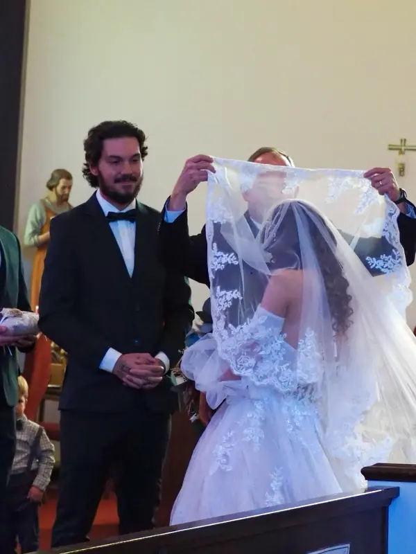 Groom smiling as the bride's lace veil is lifted at the altar